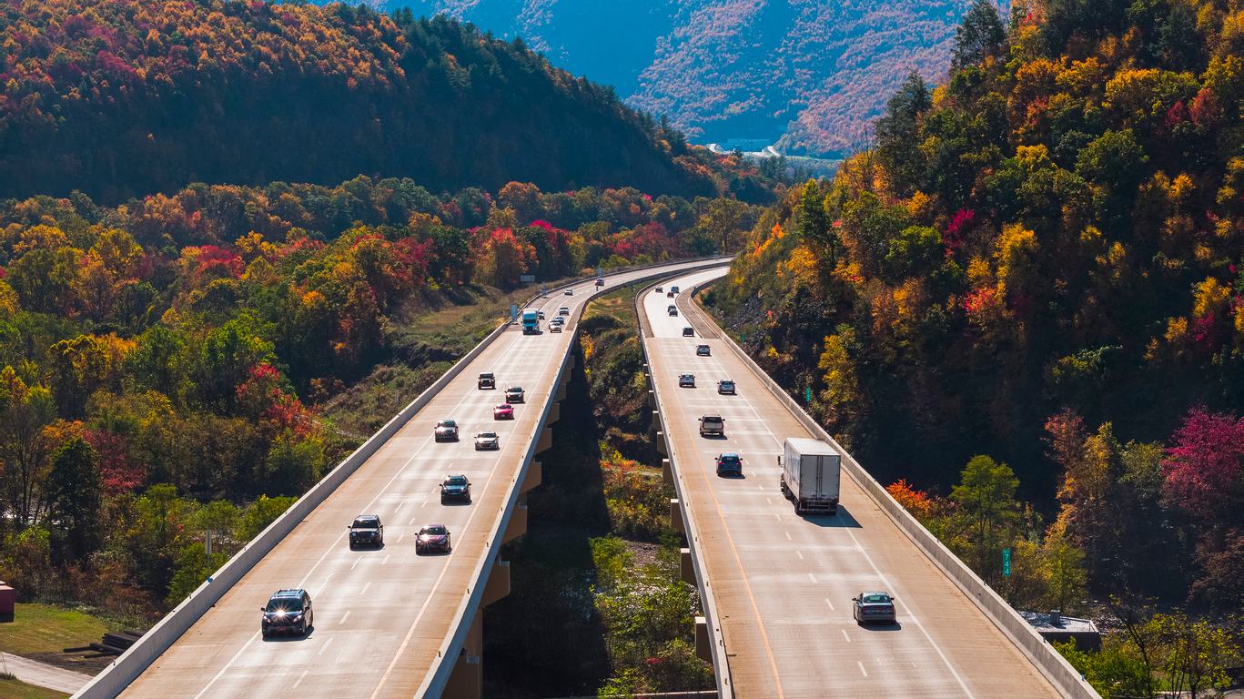 Cars and trucks traveling along a divided highway through autumn mountains